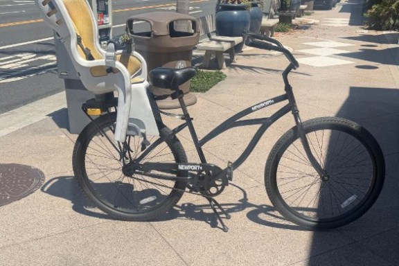 Black bicycle with a child seat parked on a sunny city sidewalk.