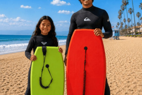 Two people on a beach holding surfboards, one red, one green, under a clear blue sky.