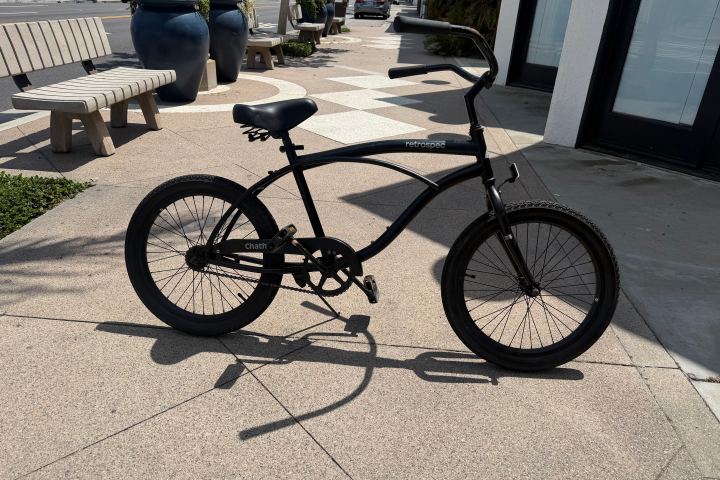 Black bicycle parked on a sidewalk near benches and planters.