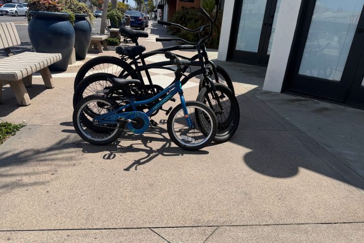 Three bicycles, including a child's bike, parked on a sunny sidewalk.