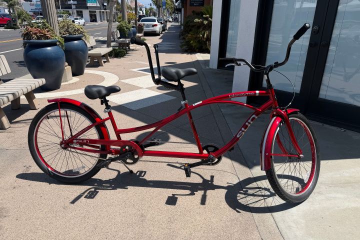 Red tandem bicycle parked on a sunny sidewalk.